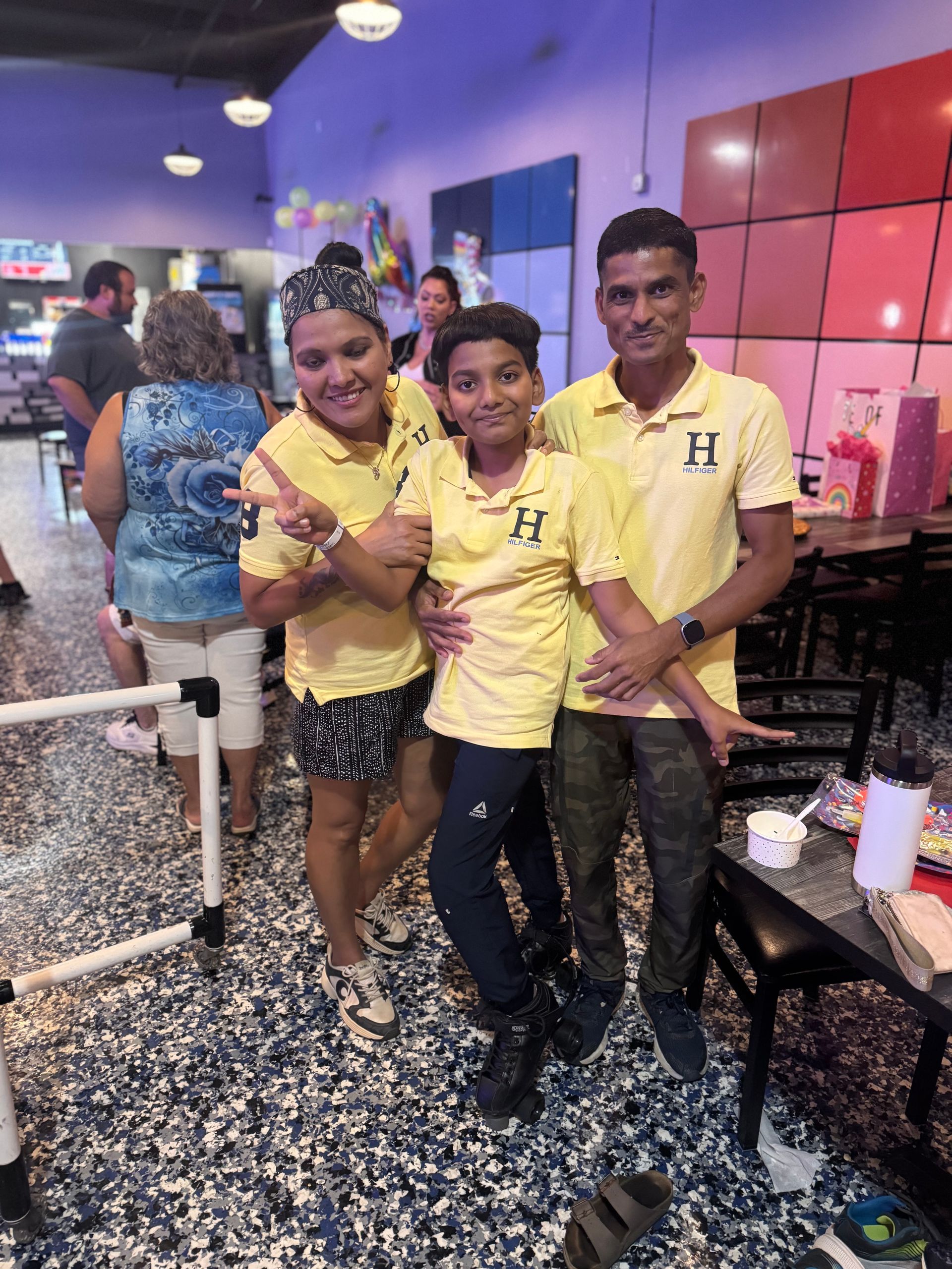 Family in yellow shirts pose indoors. Boy in the middle, two adults on either side, possibly at a restaurant.