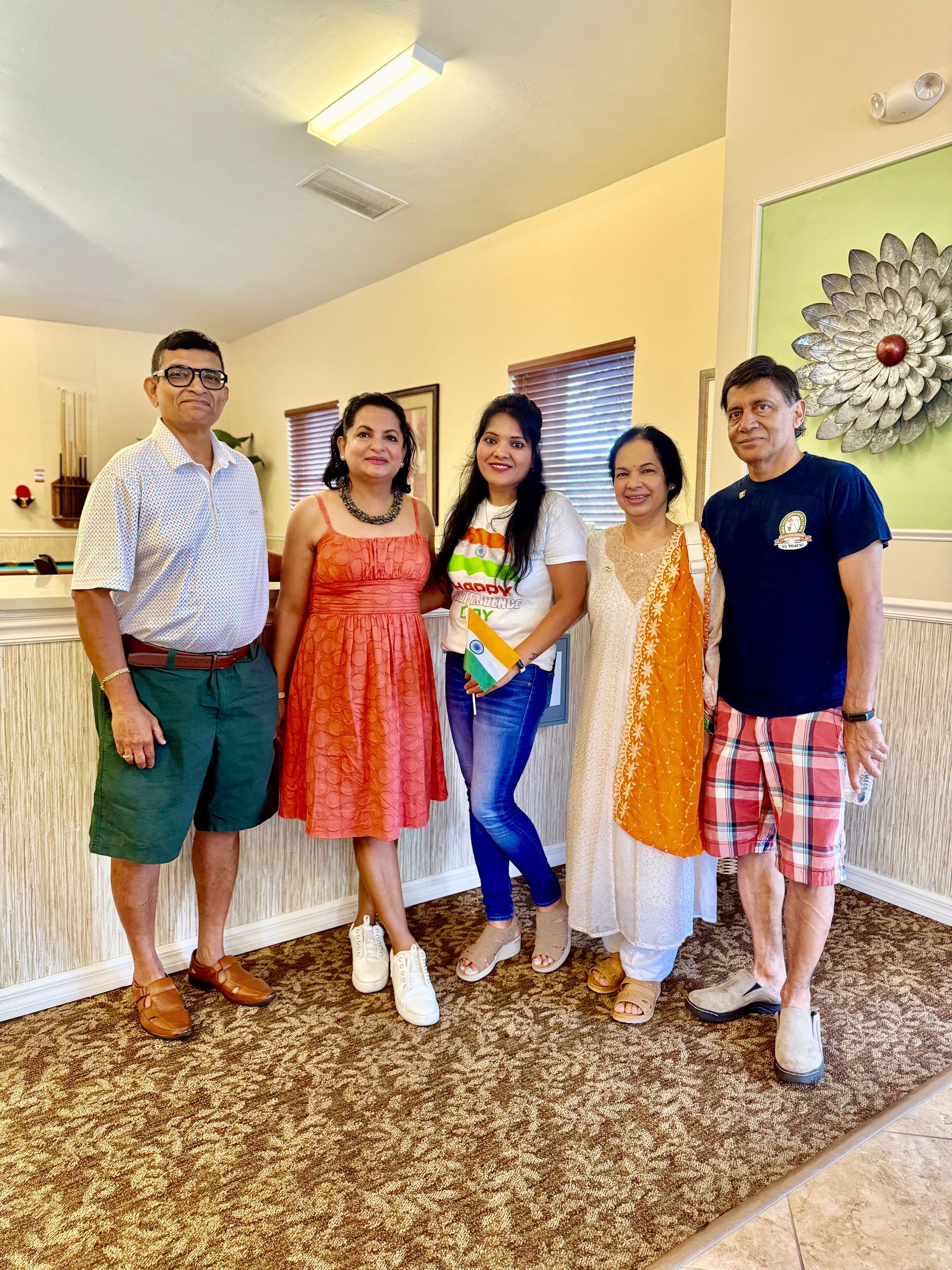 Five people pose together indoors. One wears orange and white Indian flag sash.