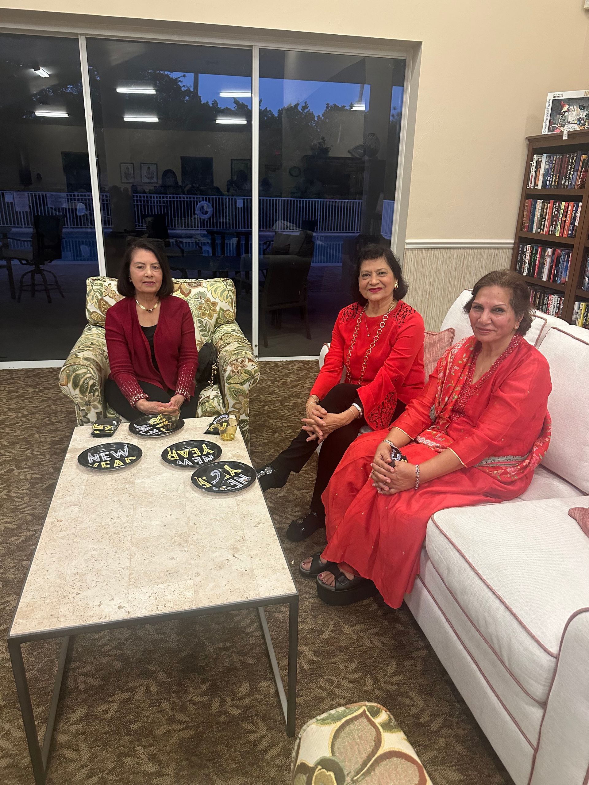 Three women in red outfits sitting in a living room, one on a sofa, others in armchairs.