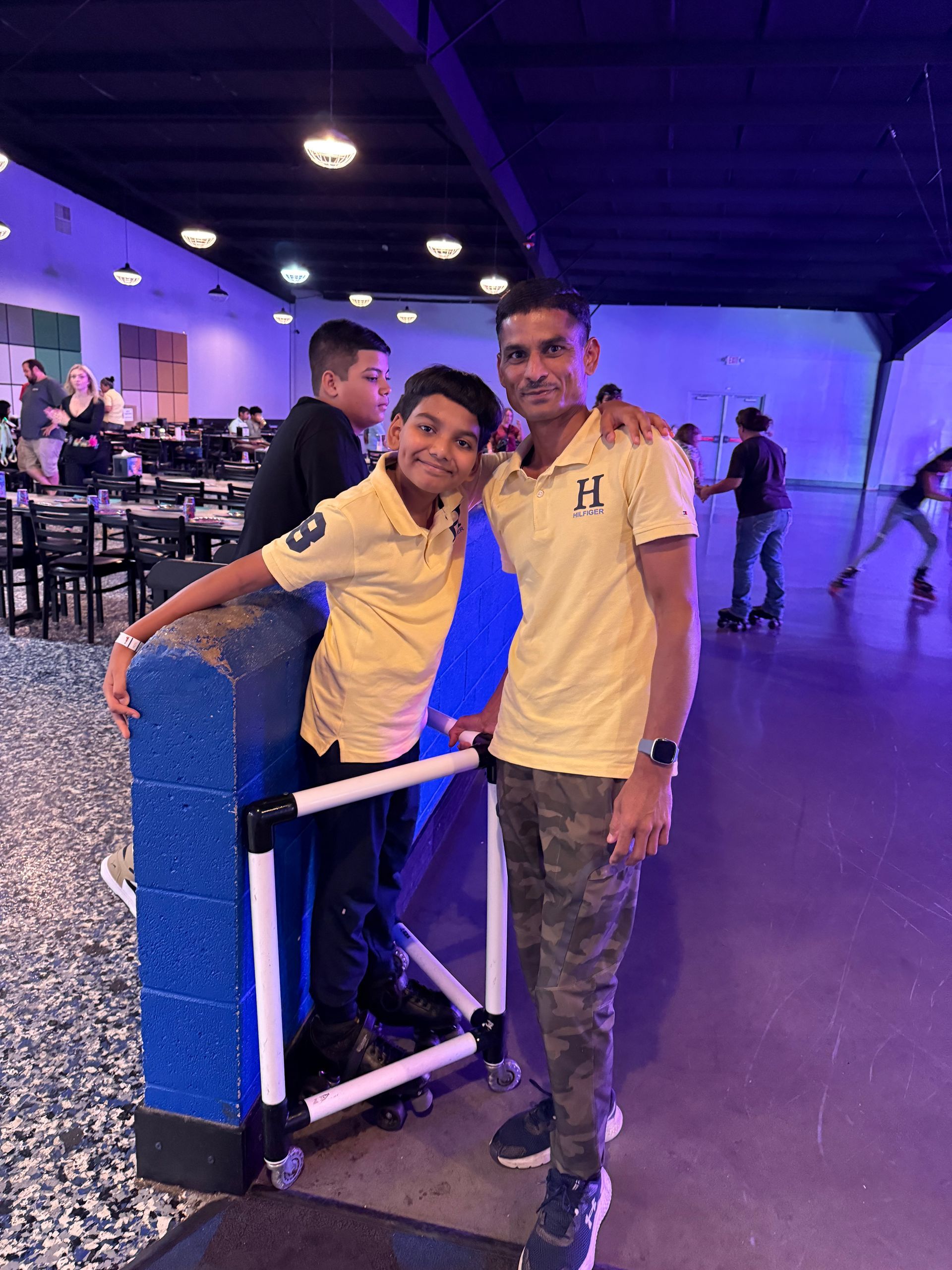 Two people in yellow shirts pose at a roller-skating rink. One has arm around the other.