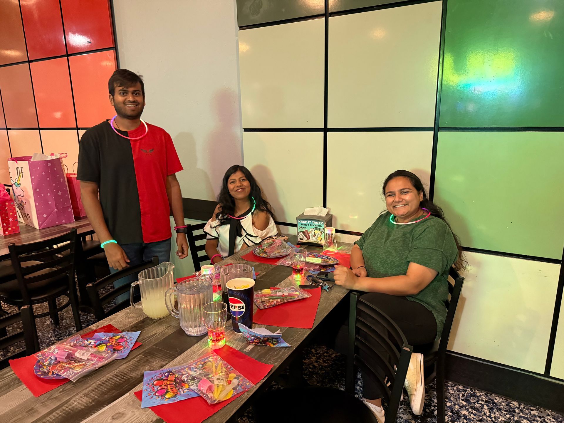 Three people at a table in a restaurant, smiling. Decorations and gifts are visible.