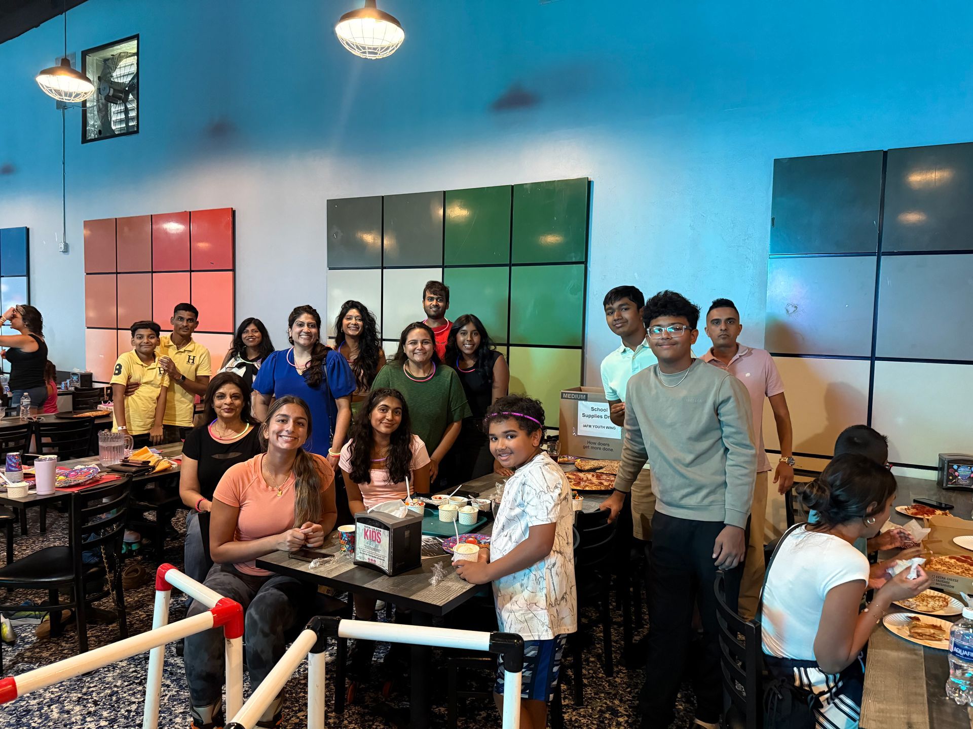 Group of people at a restaurant, smiling and posing, with colorful wall blocks.