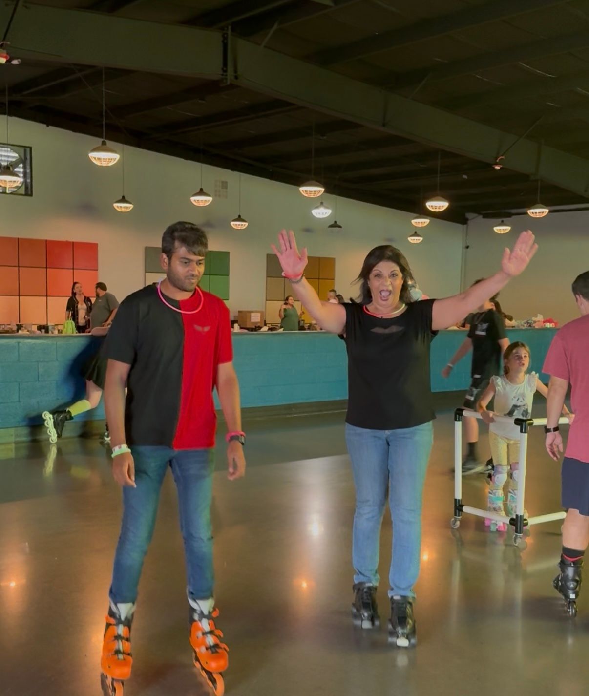 Man and woman roller skating indoors; woman with arms outstretched, man looking on.