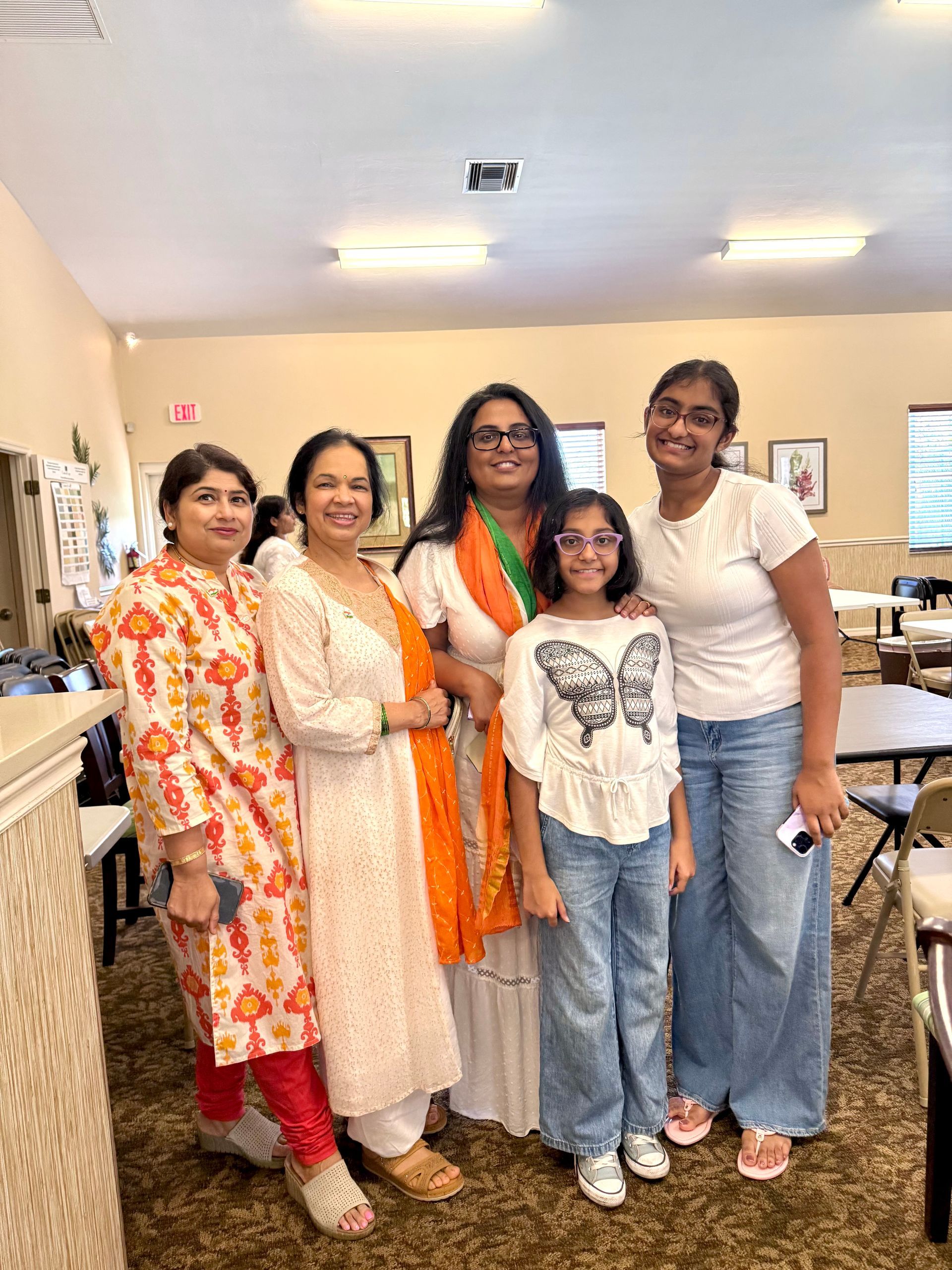 Five people pose indoors; women and a girl in white and orange clothing.