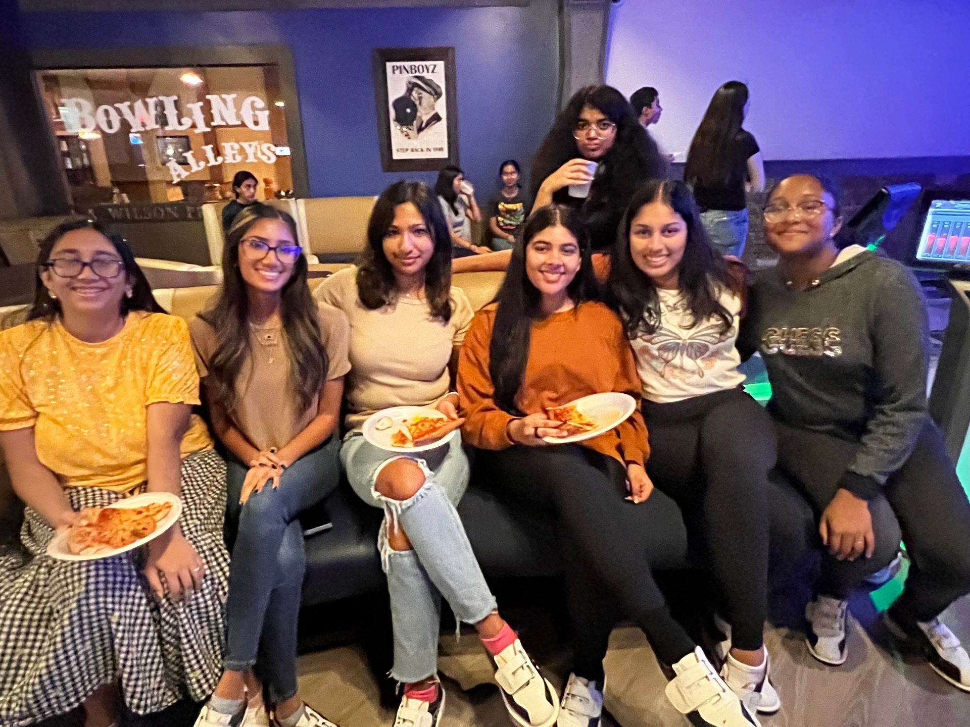 A group of young women are sitting on a couch eating pizza.