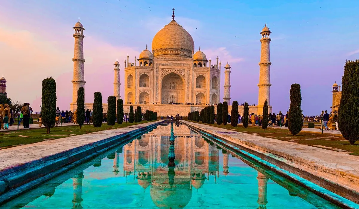 The taj mahal is reflected in the water at sunset.