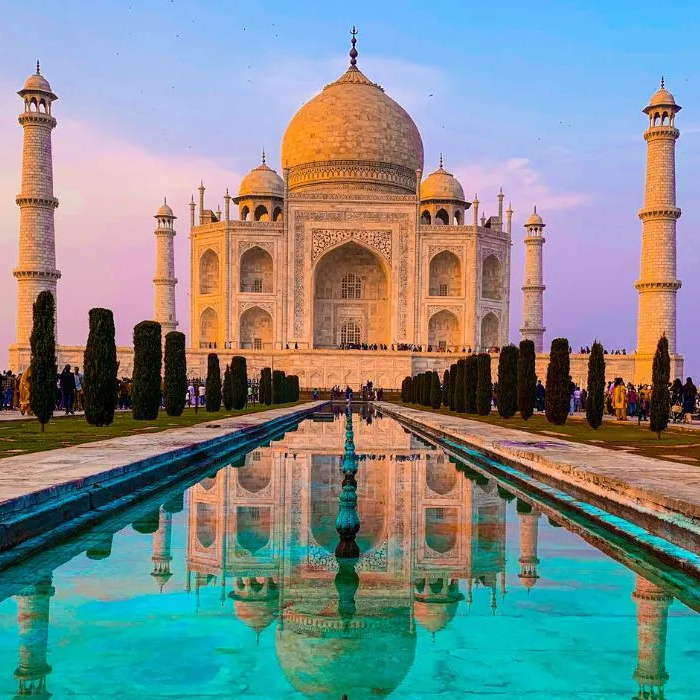 The taj mahal is reflected in the water at sunset.