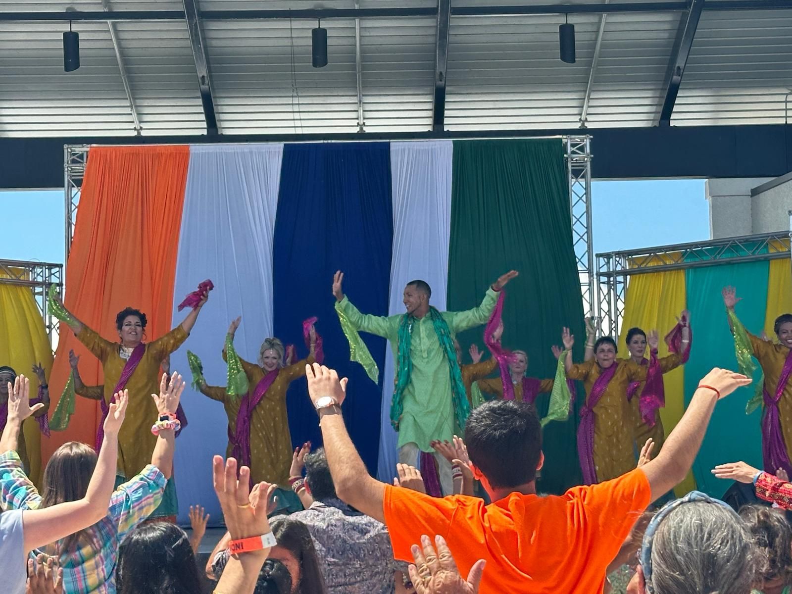 Group of people performing Indian dance on stage with the Indian flag backdrop.