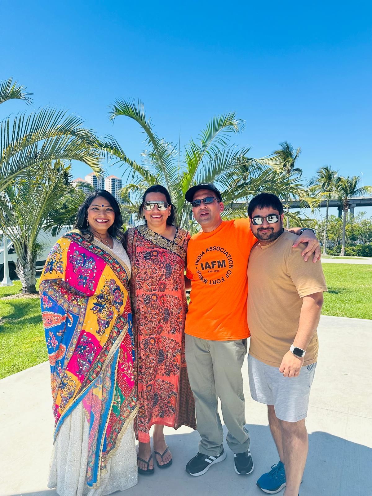 Four people smiling outdoors under a blue sky.  Two women and two men. Palm trees in the background.