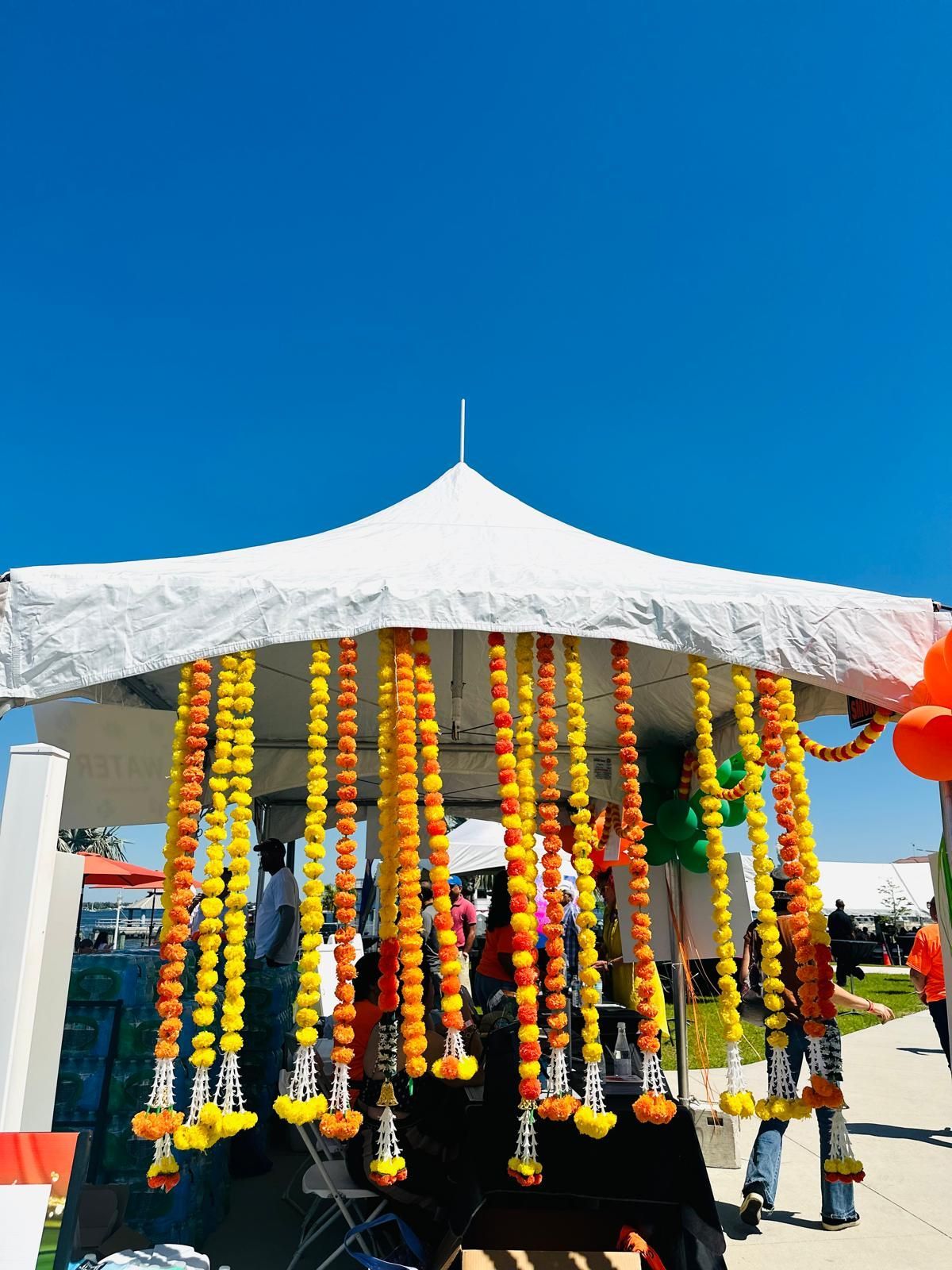 White tent decorated with orange and yellow flower garlands against a bright blue sky.