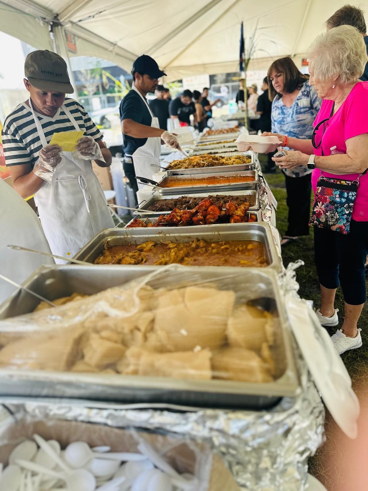 People serving and getting food from a buffet at an outdoor event.