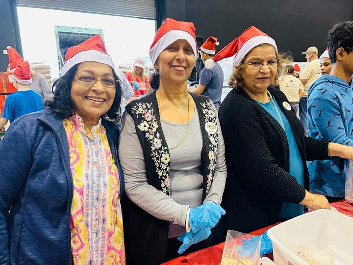 Three women wearing santa hats and gloves are standing next to each other.