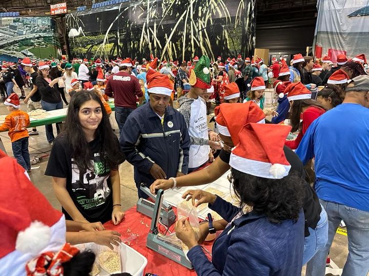 A group of people wearing santa hats are standing around a table.