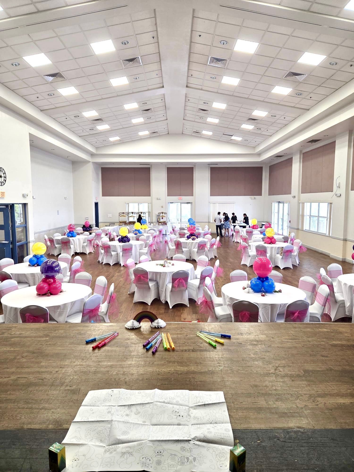A large event hall set up with round tables, decorations, and people in the background.