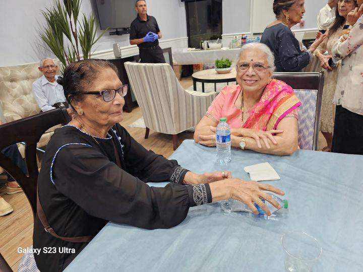Two older women are sitting at a table with a bottle of water.