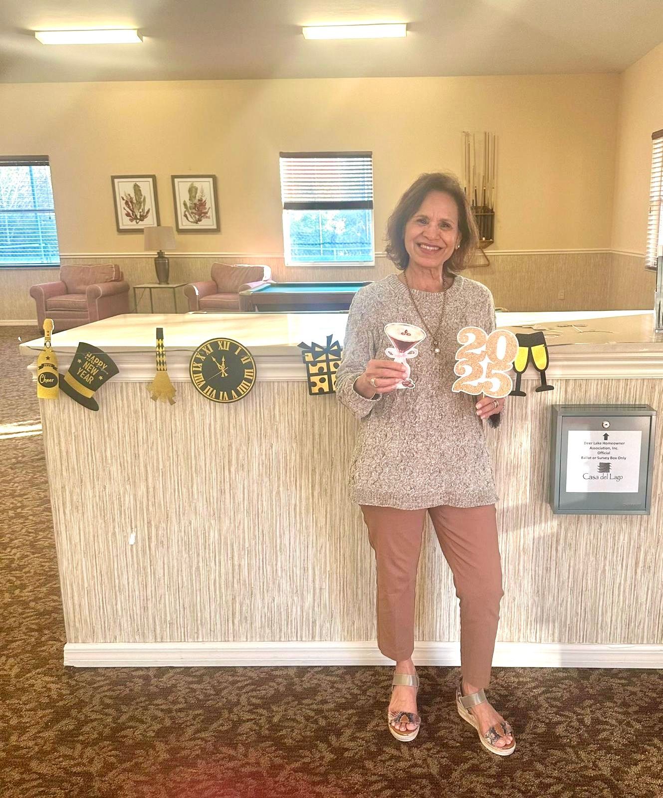 Woman in tan sweater and pink pants holding champagne glass and 
