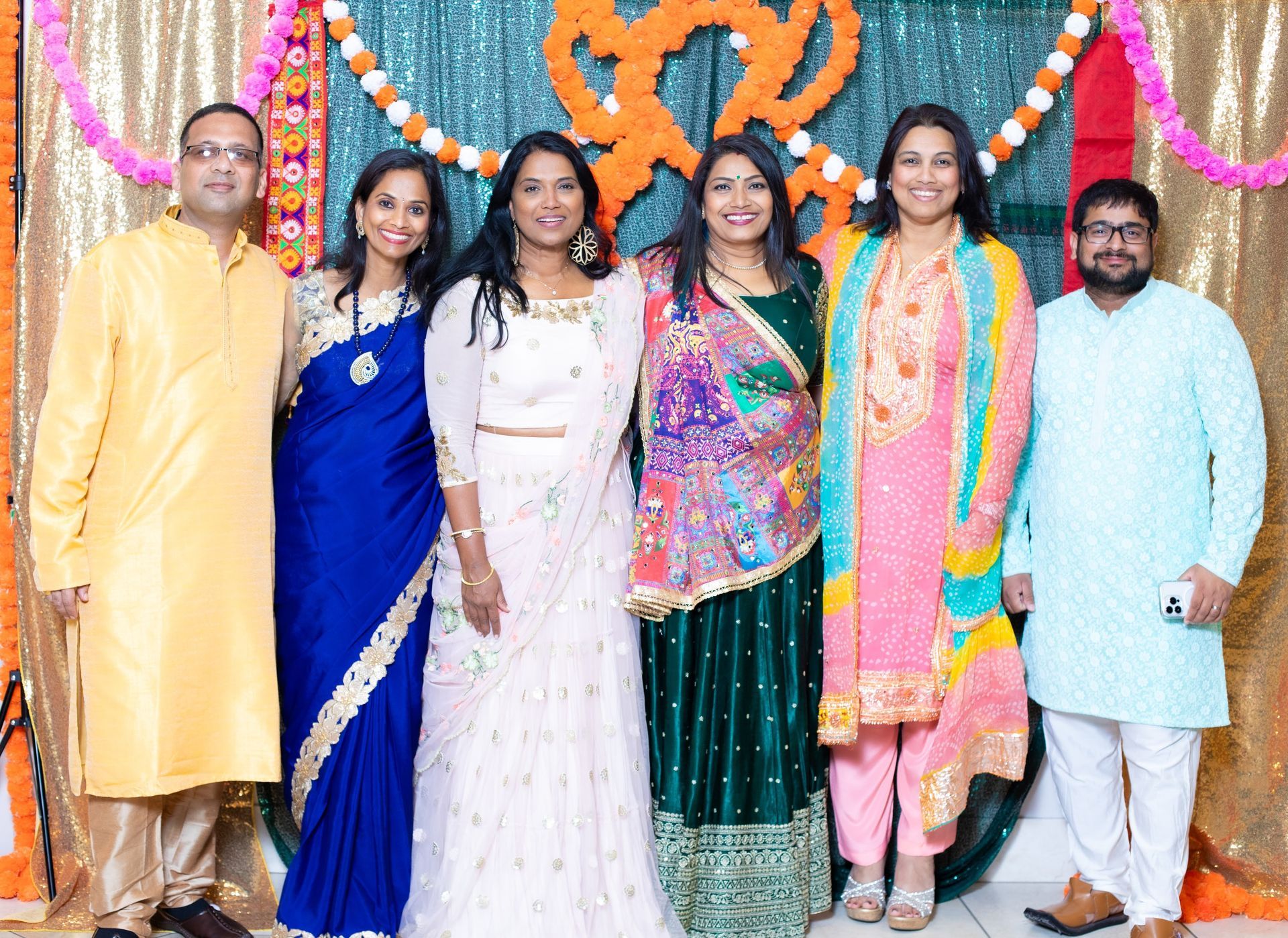 Group of six people in colorful Indian attire posing at a celebration.