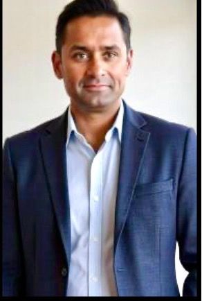 Man in a navy blazer and light blue shirt, looking at the camera.