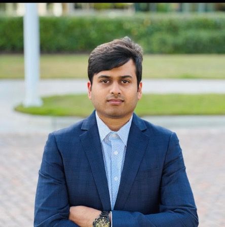 A man in a blue suit crosses his arms, standing outside.