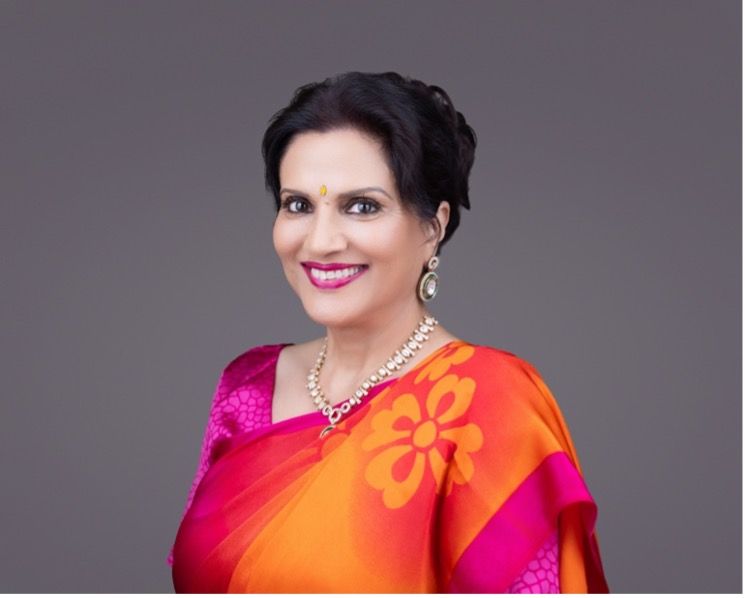 Woman in a vibrant sari, smiling, with jewelry, against a gray background.