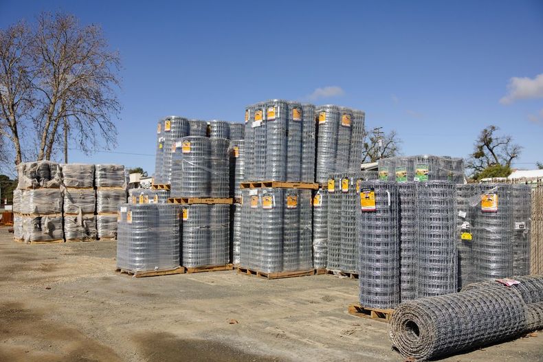 Stacks of wire fencing nd bundled materials in a dusty yard under a clear blue sky.