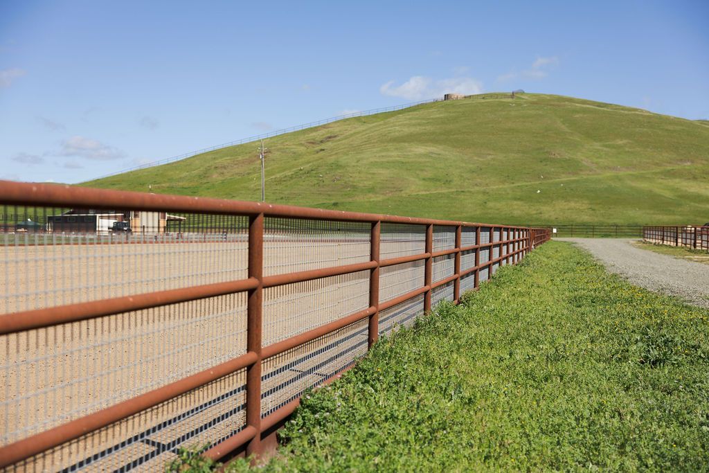 Fence beside a green hillside under a blue sky, with a gravel path along the right side
