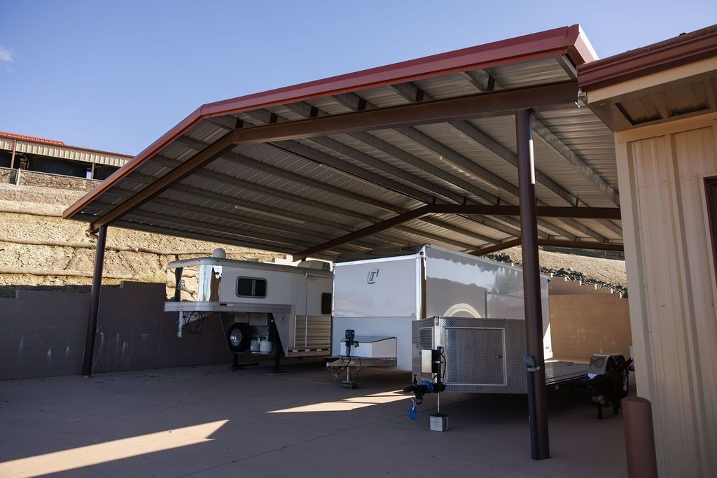 Covered outdoor yard with a parked RV, trailer, and equipment under a metal carport.