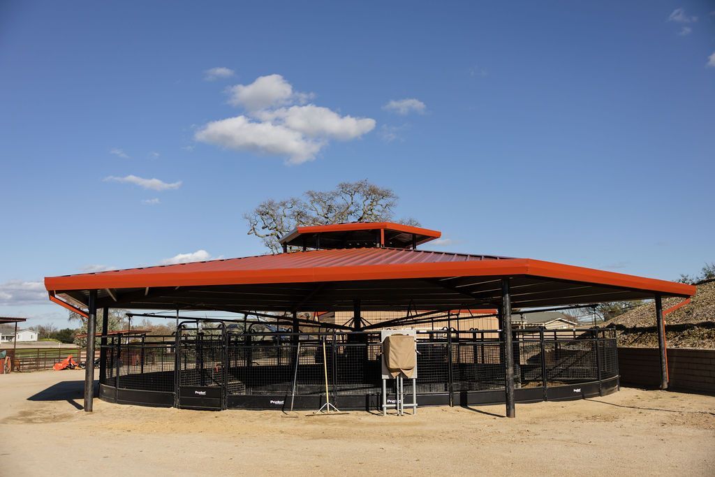 Round, open-air shelter with an metal roof in a dry, sandy landscape under a blue sky.