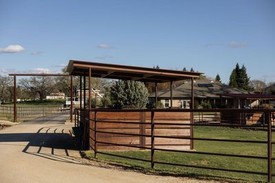 Wooden animal pens and a covered shelter in a fenced farmyard under a clear blue sky