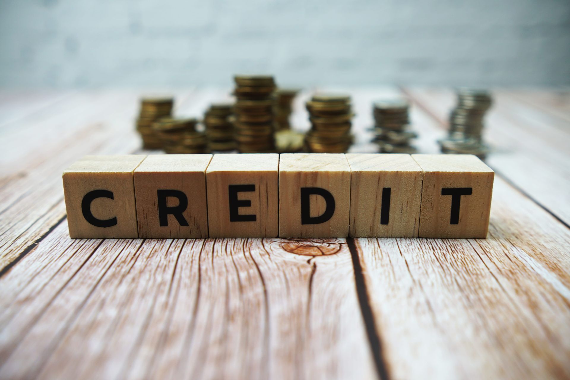 Wooden blocks spelling “CREDIT” with stacked coins in the background