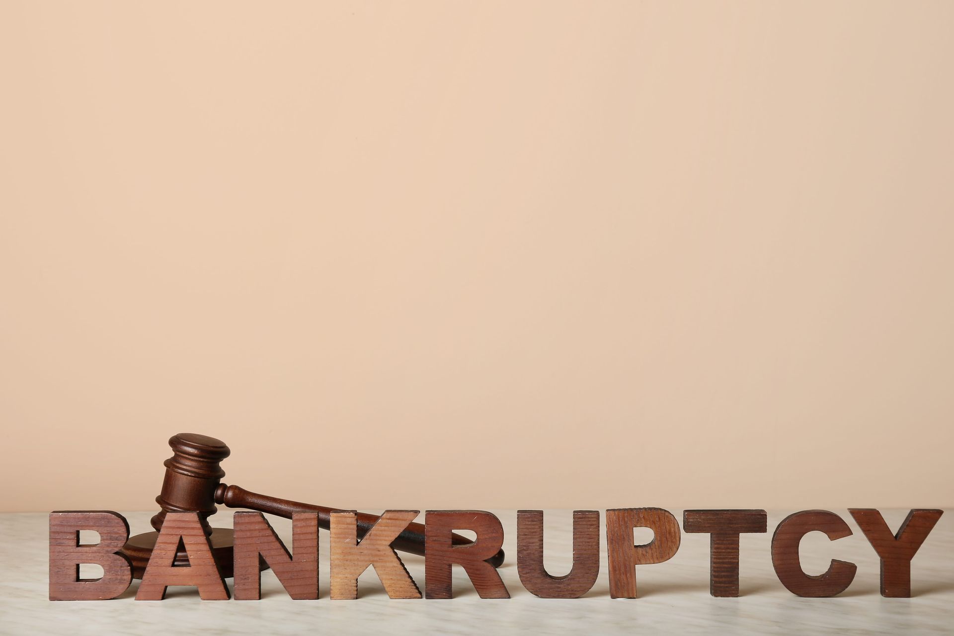 Gavel beside wooden letters spelling “BANKRUPTCY” on a neutral background