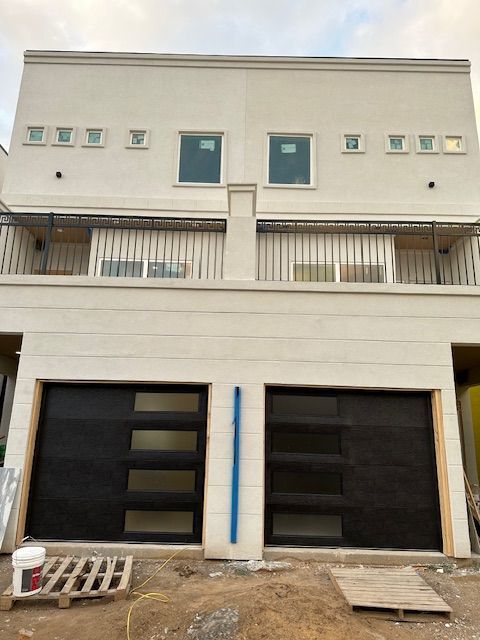 A white house with two black garage doors and a balcony.