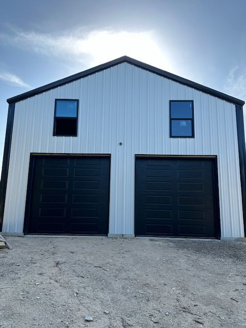 A white barn with black garage doors and windows.
