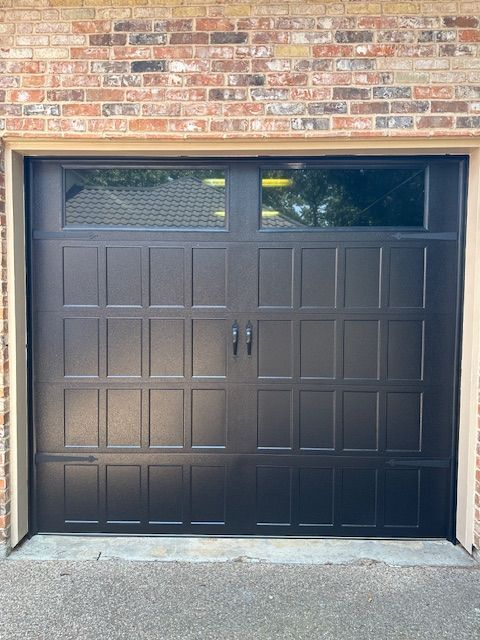 A black garage door is sitting in front of a brick building.