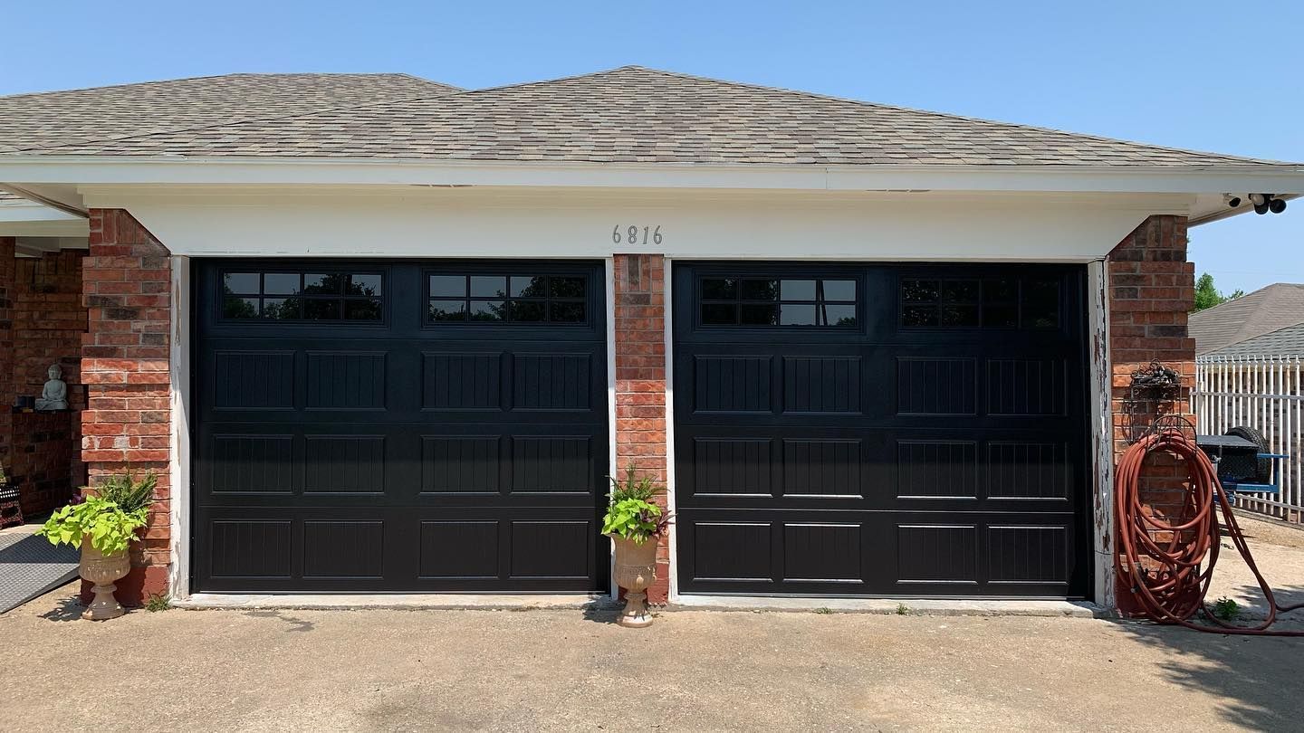 A couple of black garage doors on a brick house.