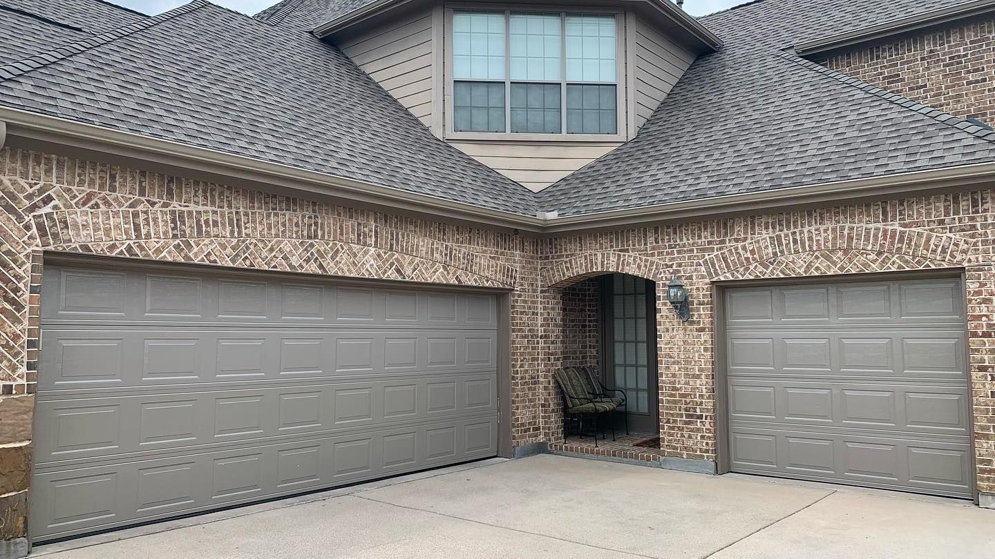 A large brick house with two garage doors and a gray roof.