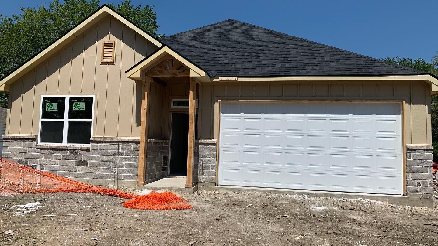 A house with a garage door is being built in a dirt field.
