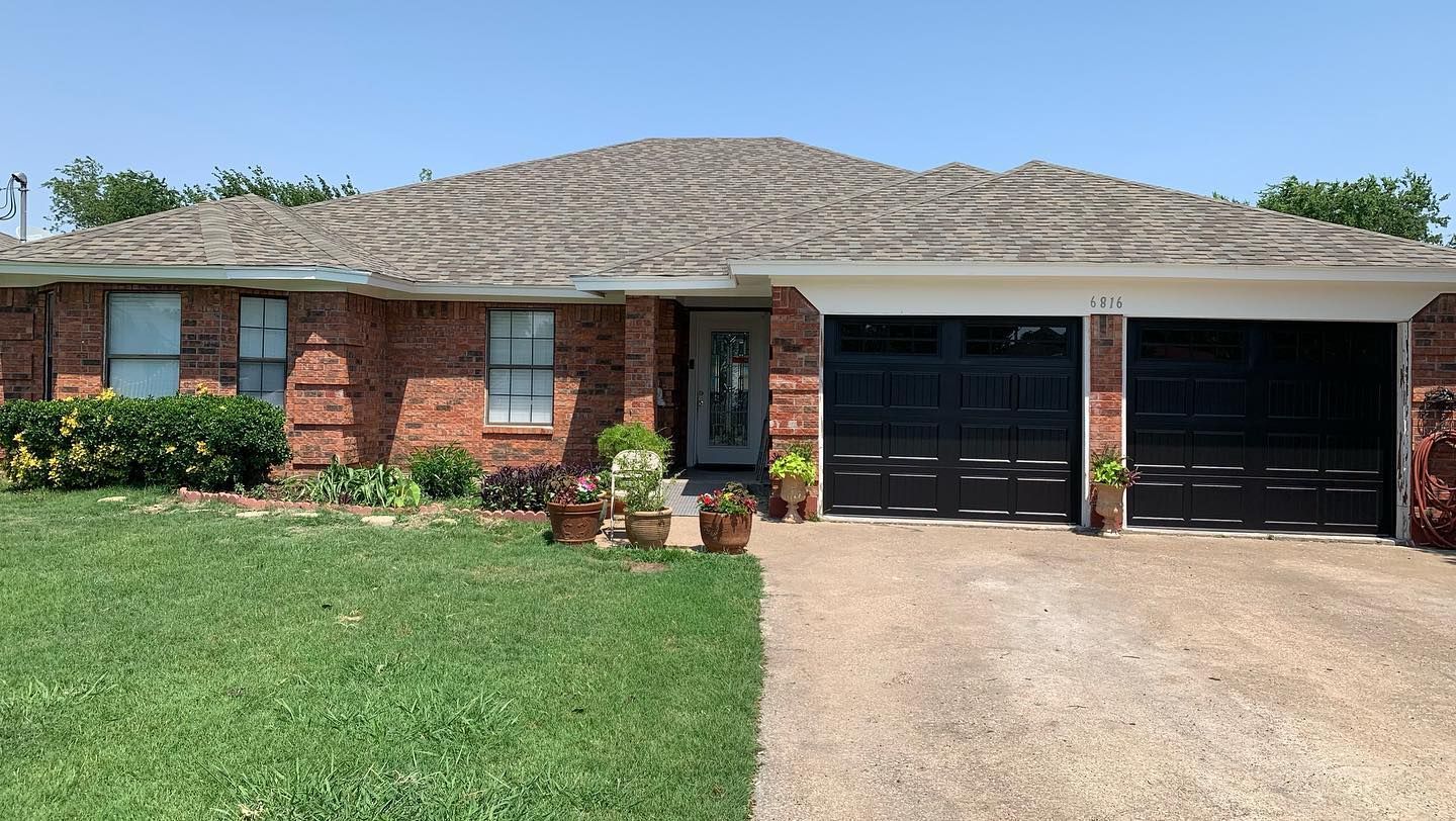 A brick house with two garage doors and a lush green lawn.
