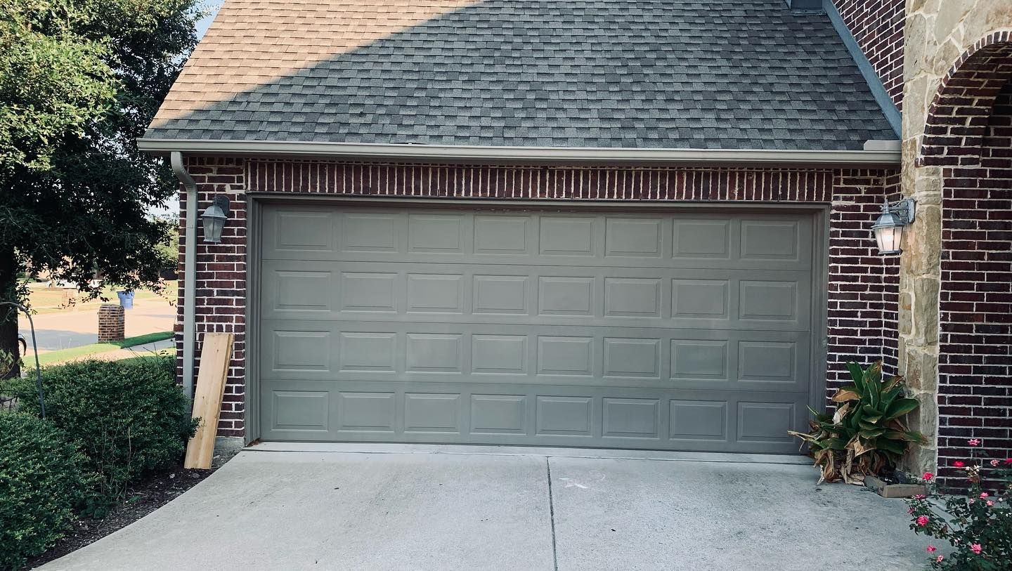 A gray garage door is sitting in front of a brick house.