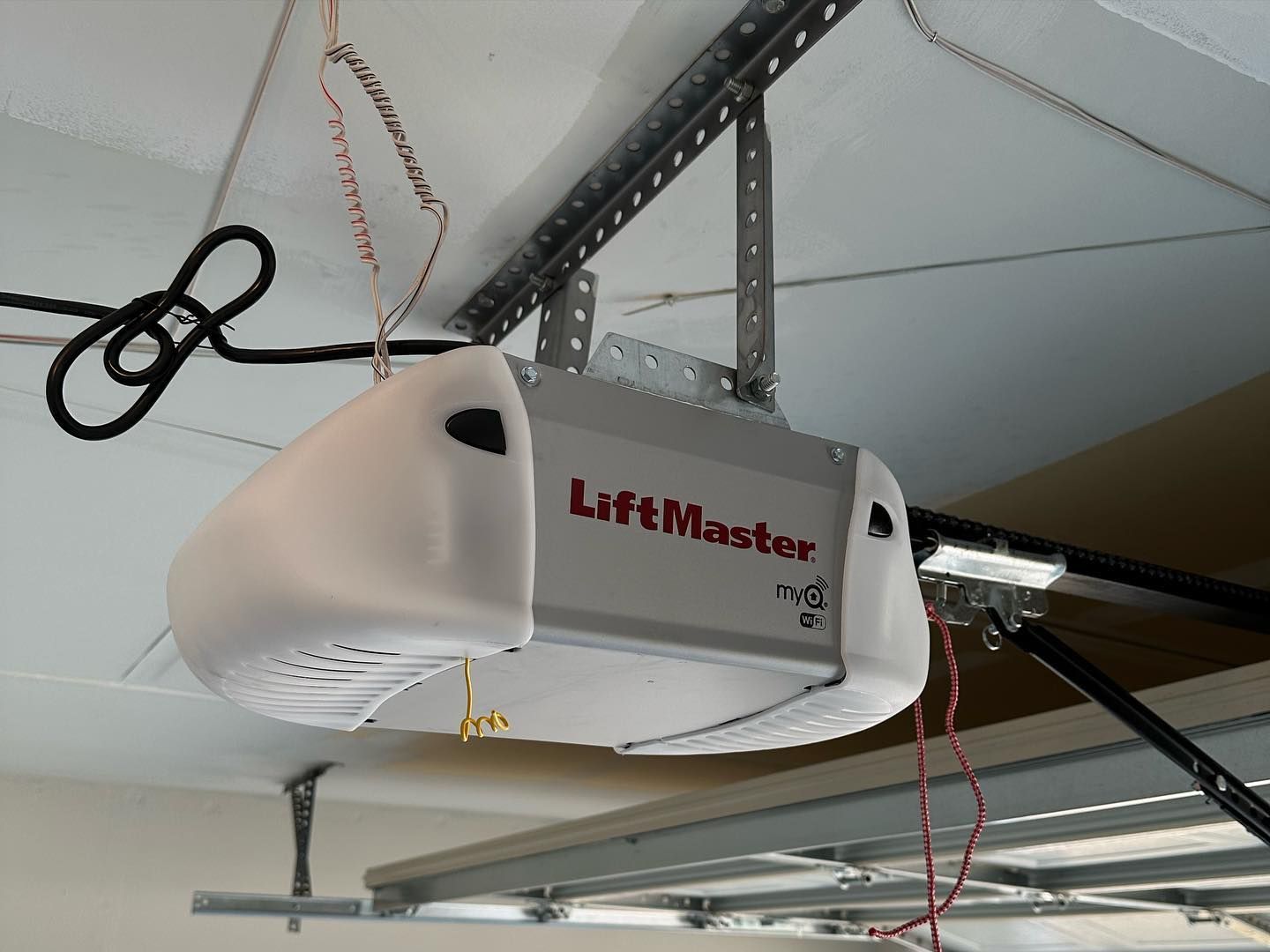 A lift master garage door opener is hanging from the ceiling of a garage.