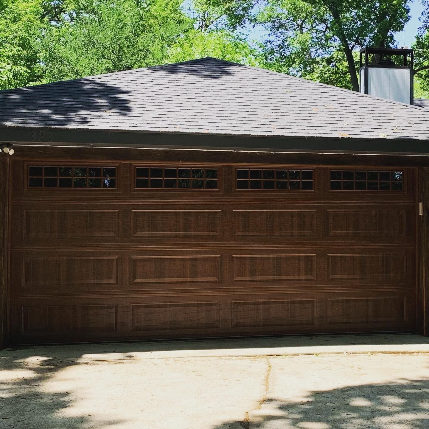 A brown garage door with a roof and trees in the background