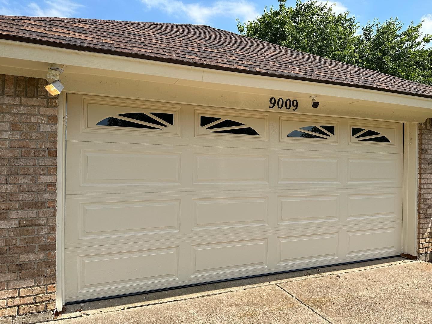 A white garage door is on the side of a brick house.
