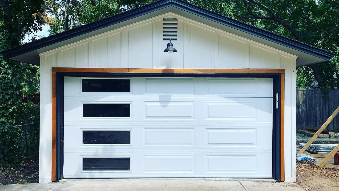 A white garage door with black stripes on it is sitting in front of a house.