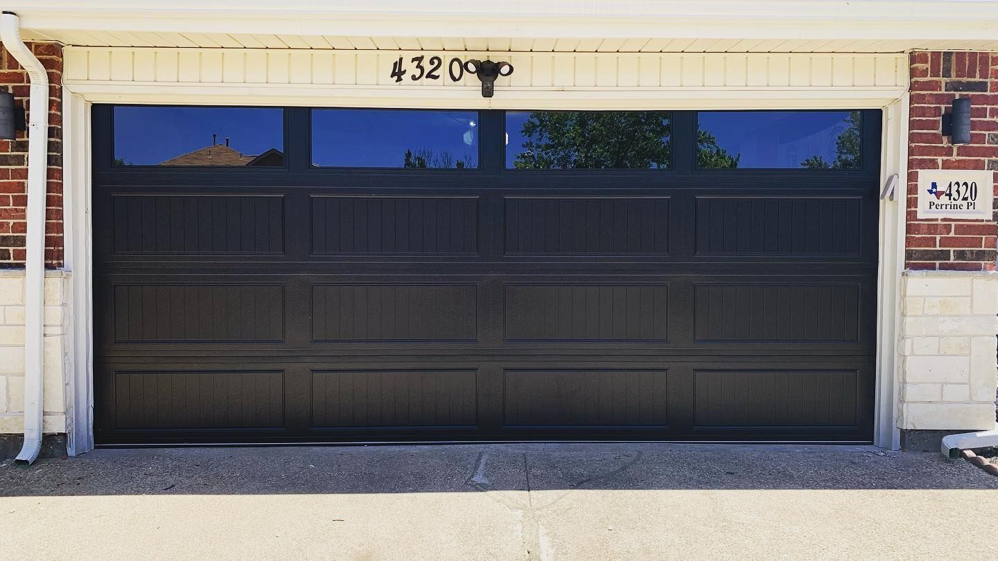 A black garage door is sitting in front of a brick house.
