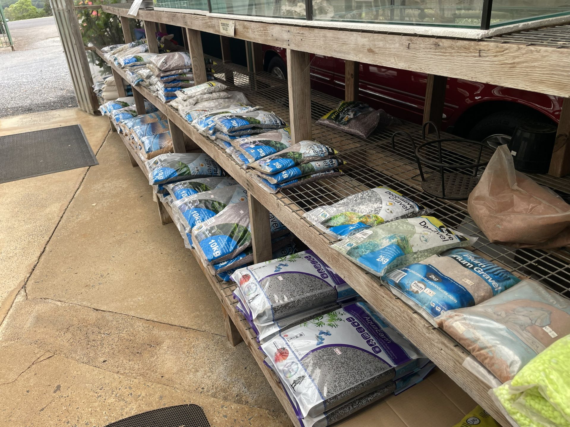 Wooden shelves stacked with bags of aquarium substrate and supplies, outdoors near a concrete floor.