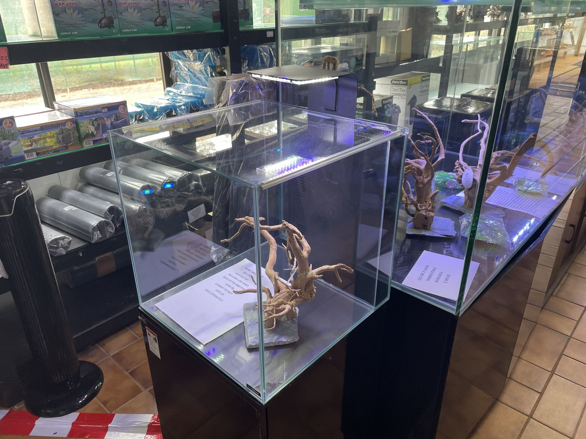 A modern fish tank display with driftwood. Black and silver with an overhead light and black cabinet stand.