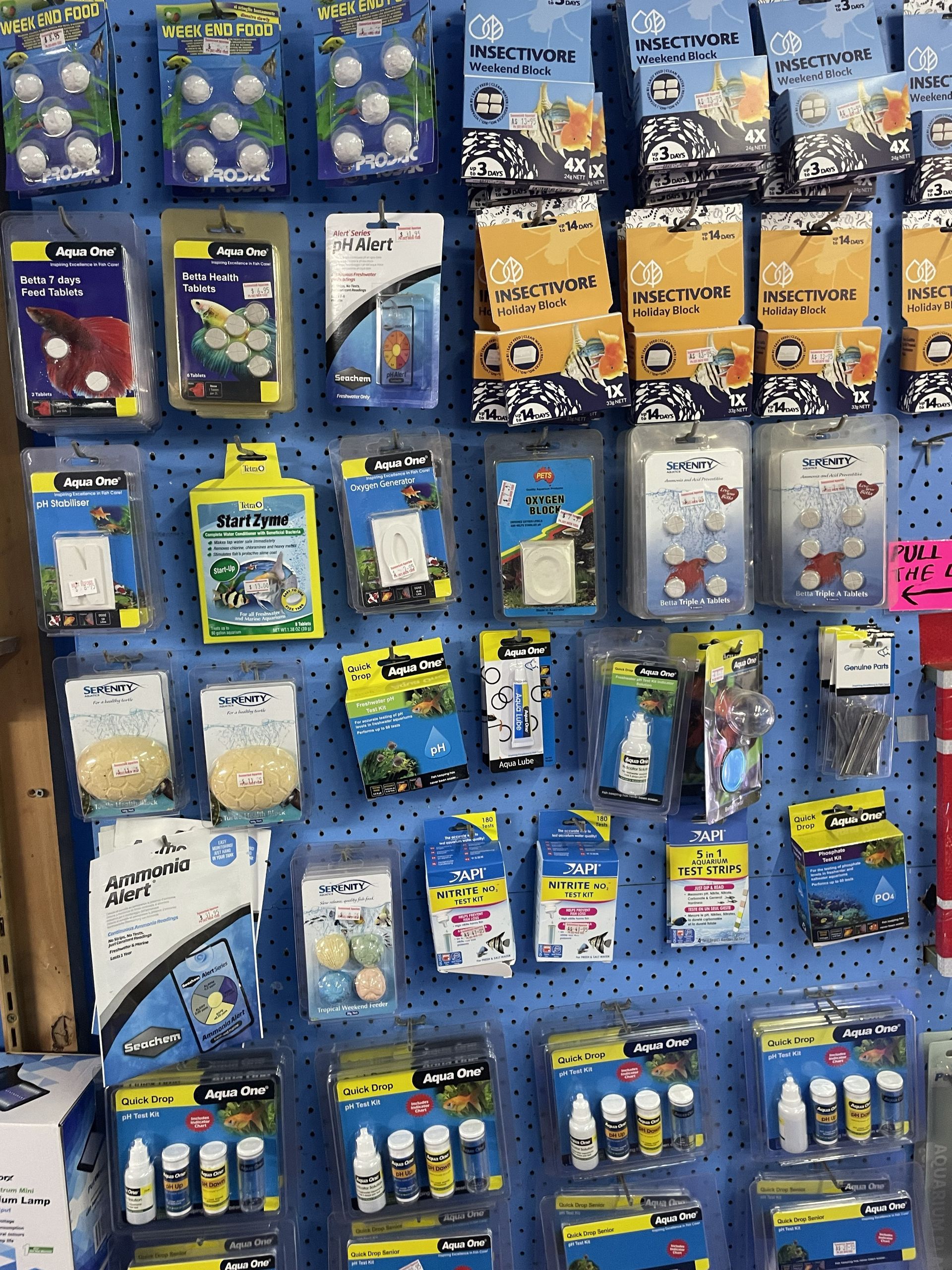 A blue pegboard displaying various packaged aquarium supplies with colorful labels.