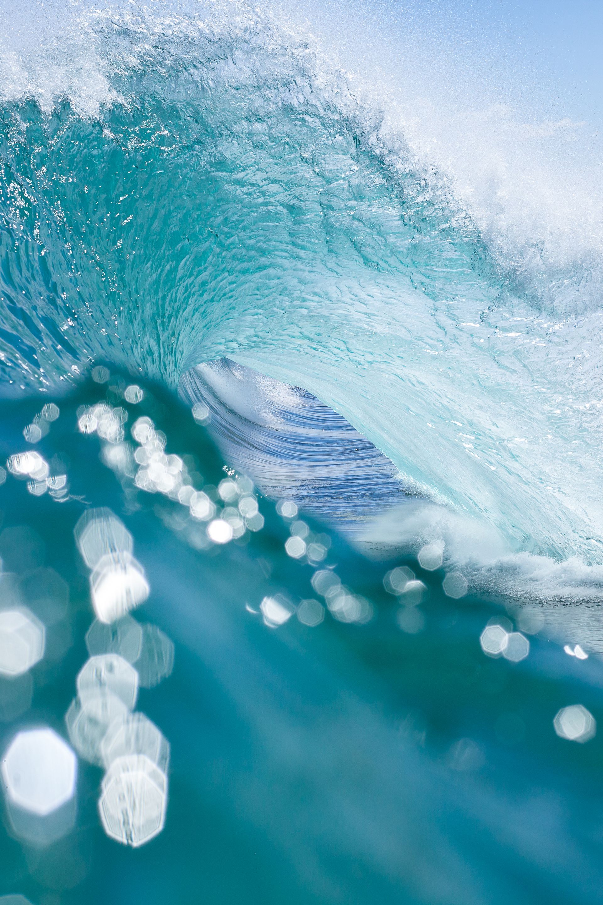 Turquoise ocean wave cresting, sunlight glistening through the water.