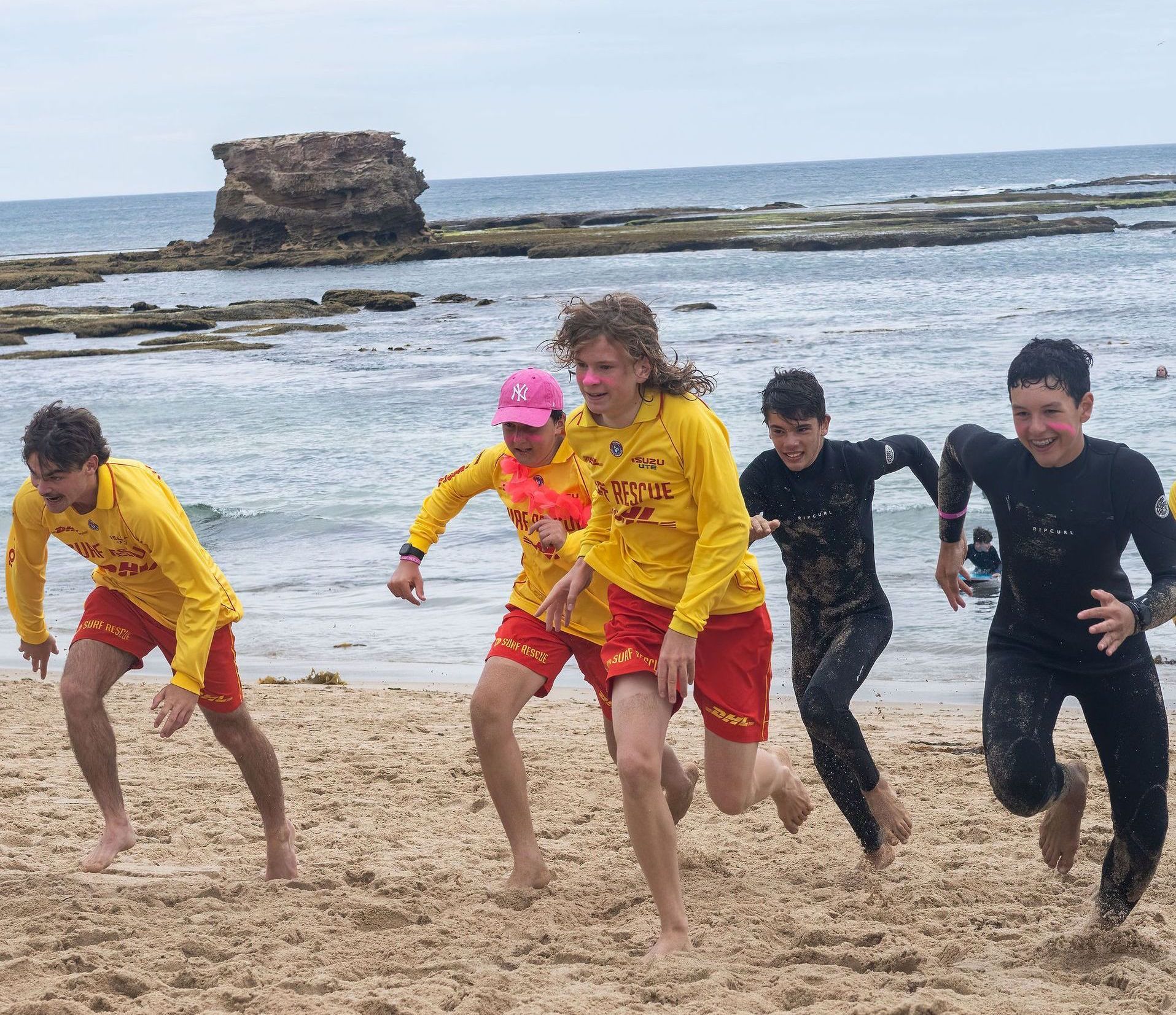 Lifeguards in yellow shirts and red shorts run on a sandy beach towards the ocean.