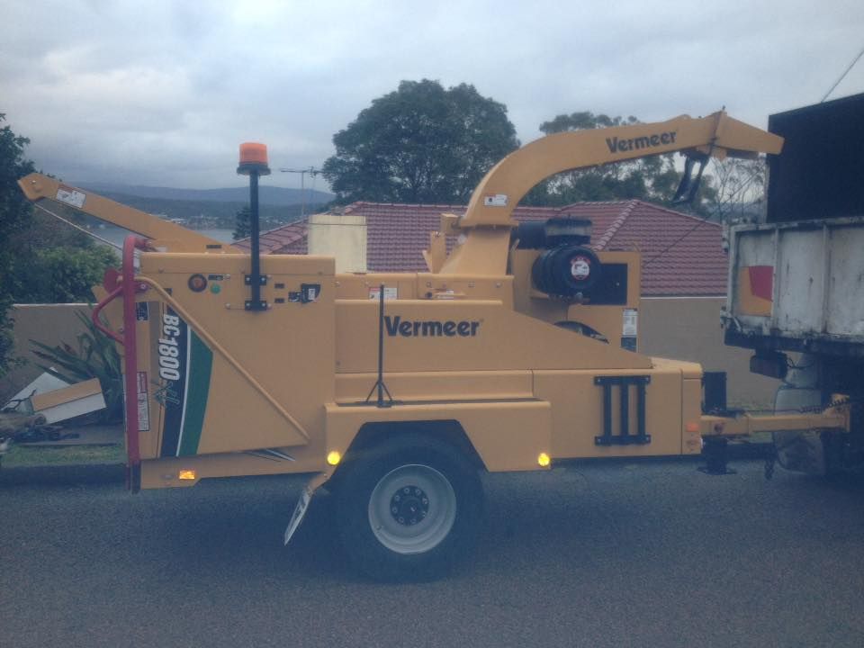 A yellow vermeer tree chipper is parked next to a truck.